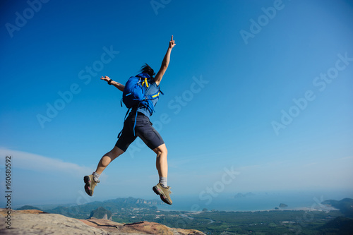 cheering woman hiker jumping on rocky mountain top