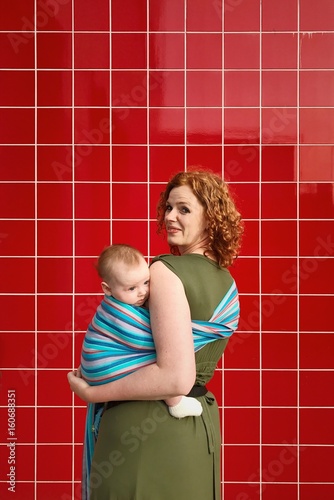 Happy mither with baby in wrap on red tails wall. photo