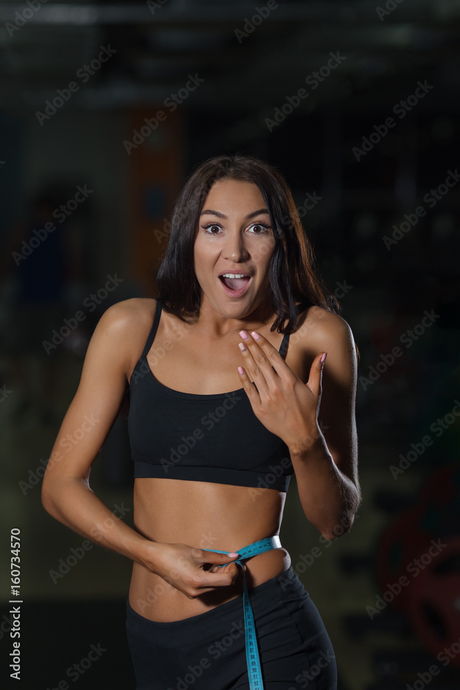 Surprised slim woman in sportswear measures waist