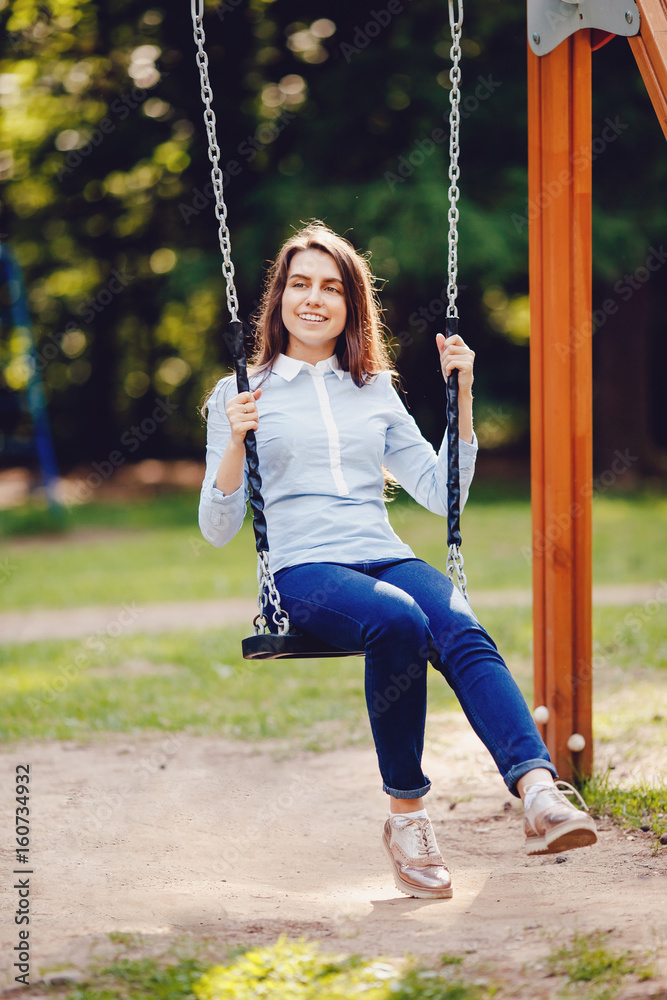 Girl student, teenager is smiling and swinging on a chain swing in the  park. Concept is a playground for rest and a happy vacation in a new place.  foto de Stock
