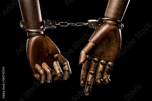 Handcuffs attach two black hands together. With copy space text. Isolated on black background. Studio Shot.