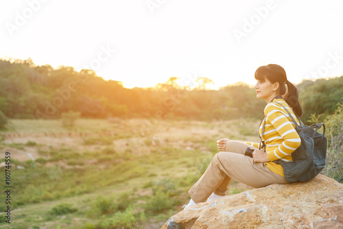 Young Woman in yellow sweater’s sitting on a giant rock for rest and watching sunset between travel in mountain for her vacation. © Arnon