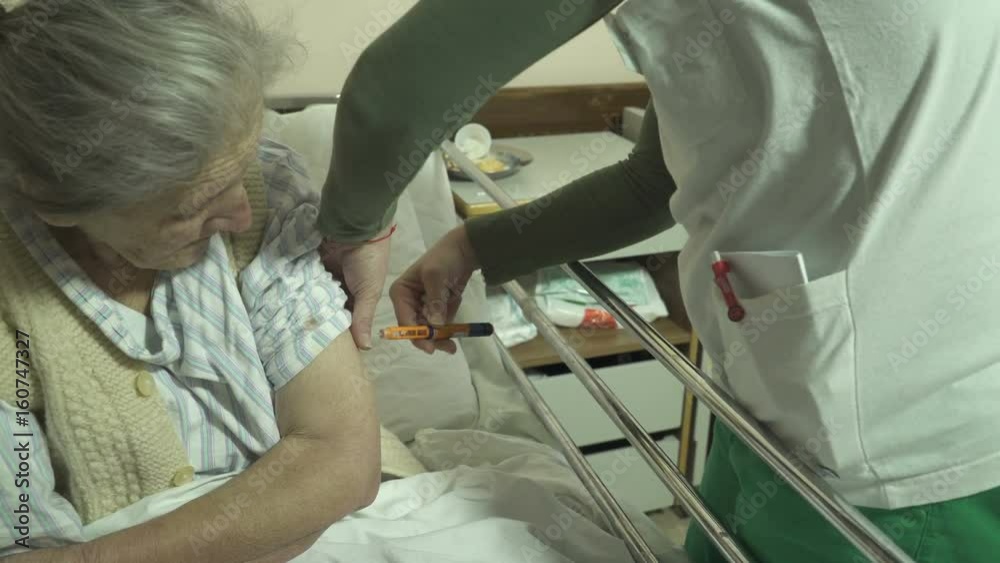 Very old woman in pajama lying in bed at hospital room while nurse injecting insulin in her arm, dolly shot, portrait of elderly female patient, treatment for diabetes, indoors Very old woman in pajama lying in bed at hospital room while nurse injecting insulin in her arm, dolly shot, portrait of elderly female patient, treatment for diabetes, indoors