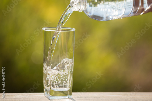 A glass of water is pouring into the glass, on the nature
