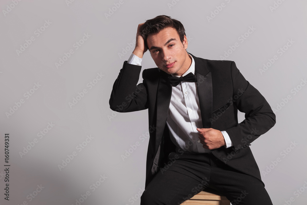 seated elegant man in tuxedo fixing his hairstyle seated elegant man in tuxedo fixing his hairstyle
