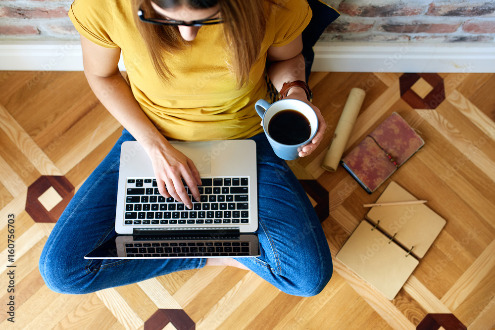 Young woman working on computer sitting on floor with cup of coffee - obrazy, fototapety, plakaty 