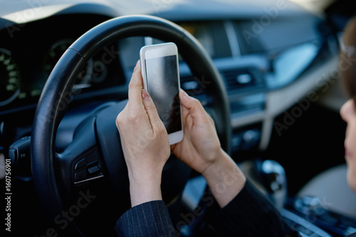 Young woman driving a car looking at the phone screen
