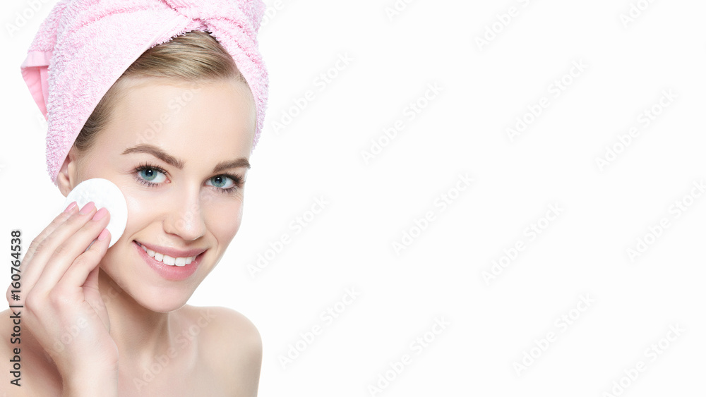 Attractive young blond woman with towel in her hair removing make up. Smiling pretty girl with perfect complexion cleansing her face using soft cosmetic cotton pad. Isolated on white background Attractive young blond woman with towel in her hair removing make up. Smiling pretty girl with perfect complexion cleansing her face using soft cosmetic cotton pad. Isolated on white background