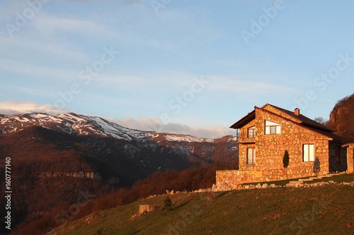 lonely stone house on the hill on the background of snowy mountains  at sunrise  horizontal