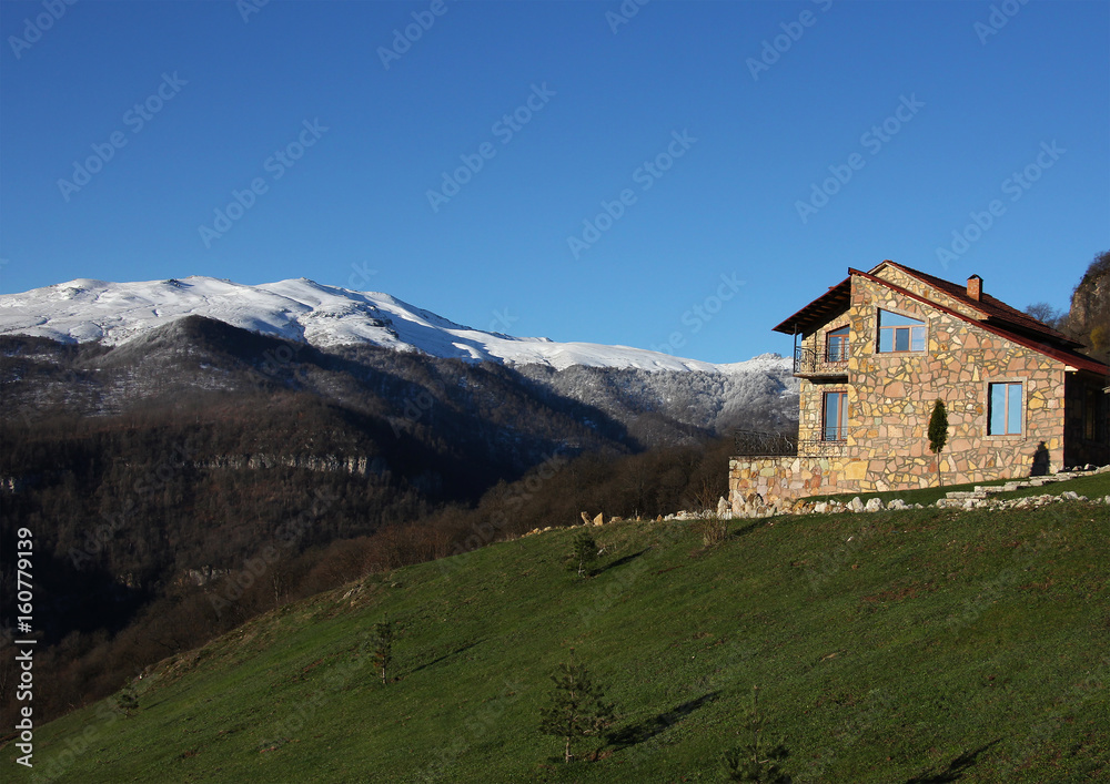 lonely stone house on the hill on the background of snowy mountains, clear blue sky, horizontal