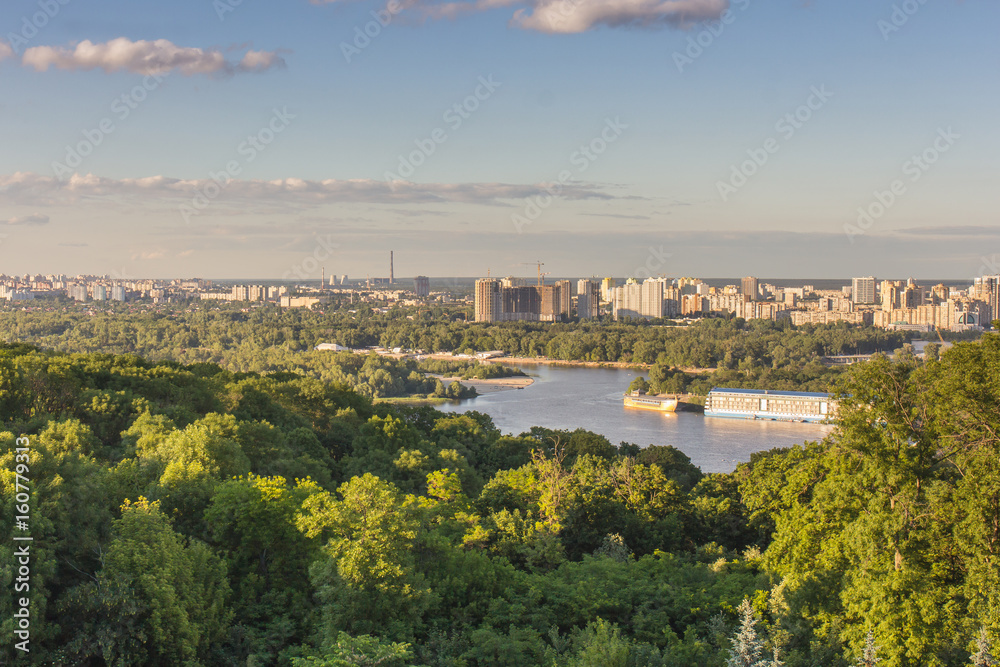 Cloudscape over the scenic cityscape of Kiev with shadows over green trees.