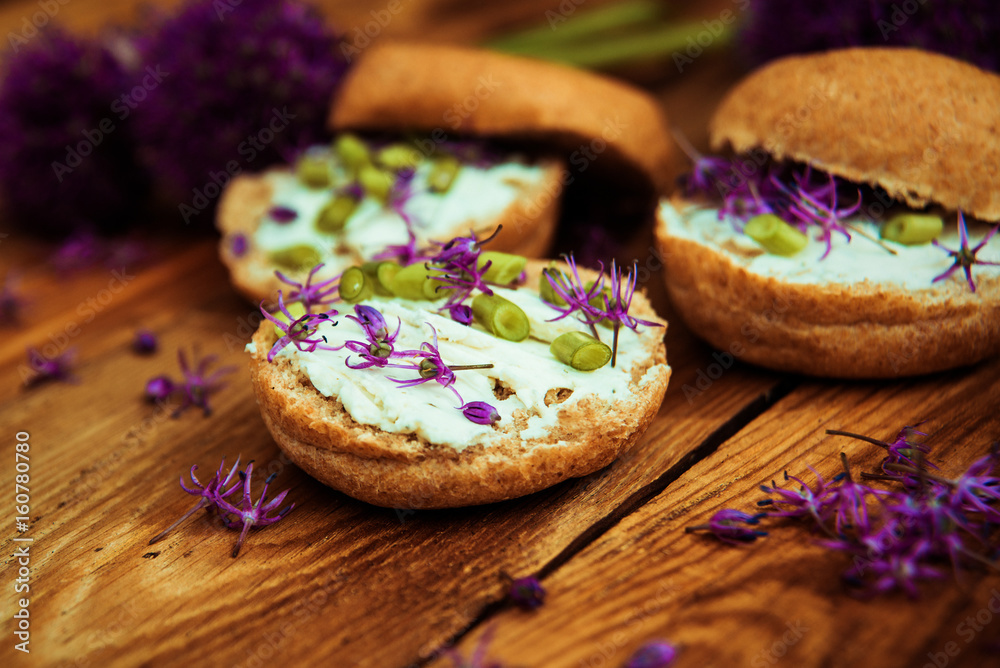 Toasted bread bruschetta with cream cheese and garlic edible flowers on olive wooden cutting board on stone slate gray background. Top view Toasted bread bruschetta with cream cheese and garlic edible flowers on olive wooden cutting board on stone slate gray background. Top view