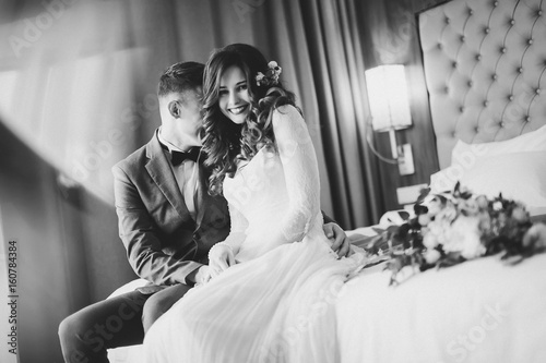Wedding shot of stylish bride and groom sitting on bed