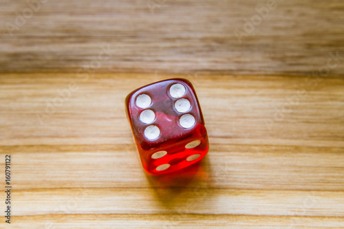 A translucent red six sided playing dice on a wooden background with number six on a top photo