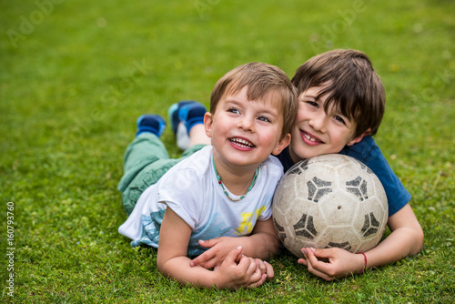 Two kids laying on the grass with a soccer ball