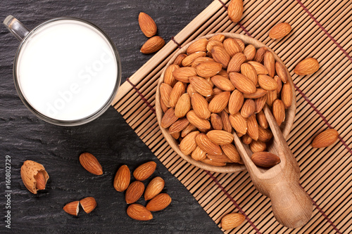 Almond milk in a glass and almonds in wooden bowl on black stone background. Top view
