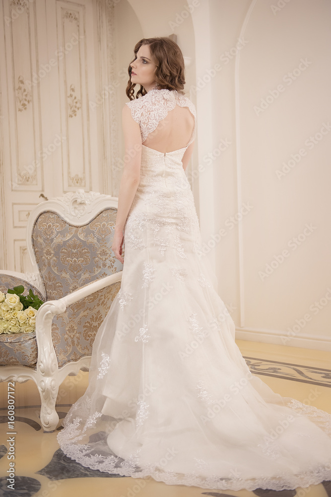 Fototapeta premium the girl is back in a wedding dress next to a vintage chair in bright room