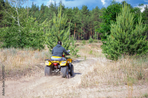 A man riding ATV on a sand road, back view