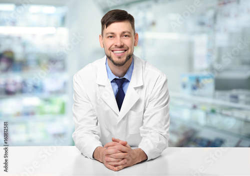 Young handsome pharmacist standing at table on white background photo