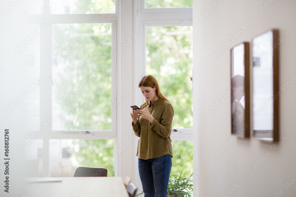 Businesswoman in empty office looking at smartphone Businesswoman in empty office looking at smartphone