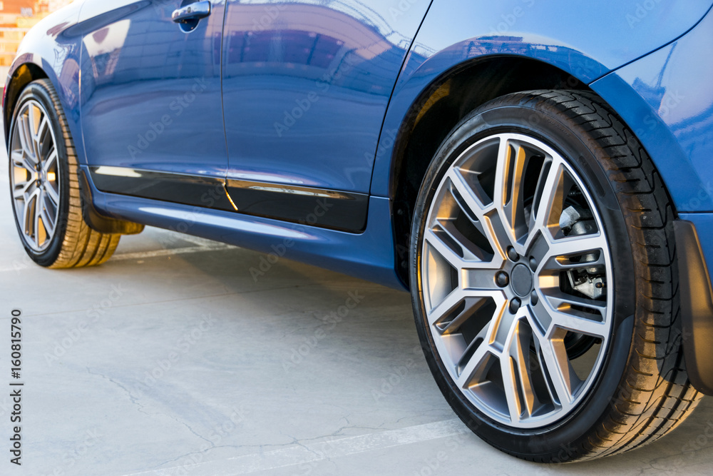 Tire and alloy wheel of a modern blue car on the ground, car exterior details