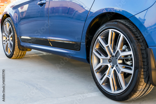 Tire and alloy wheel of a modern blue car on the ground, car exterior details