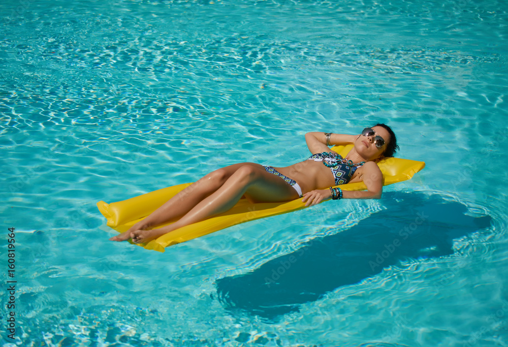 Young pretty fashion woman body posing in summer in pool with clear water lying on mattress in blue bikini and having fun