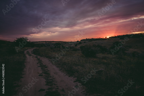 purple sunset against road with field and meadow