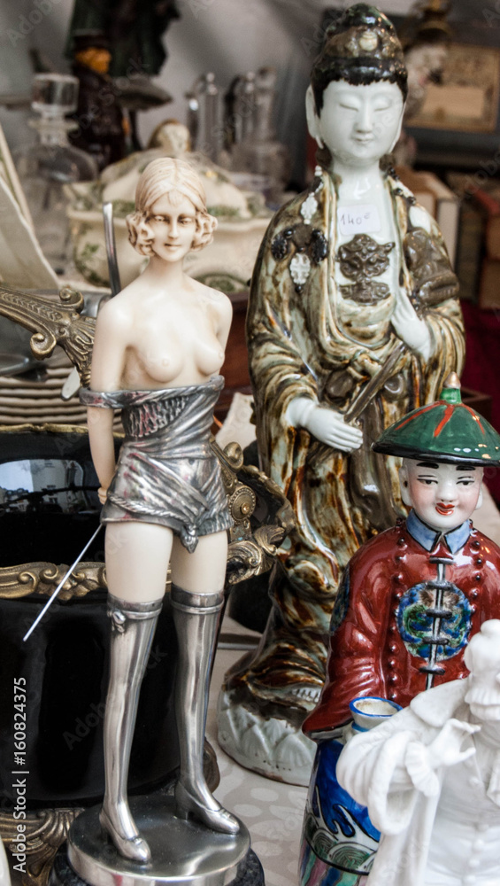 Still life at flea market in Paris (France). Seductive girl  figurine with whip and japanese figurines.