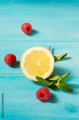 Slice of lemon, mint leaves and raspberries on a blue wooden background