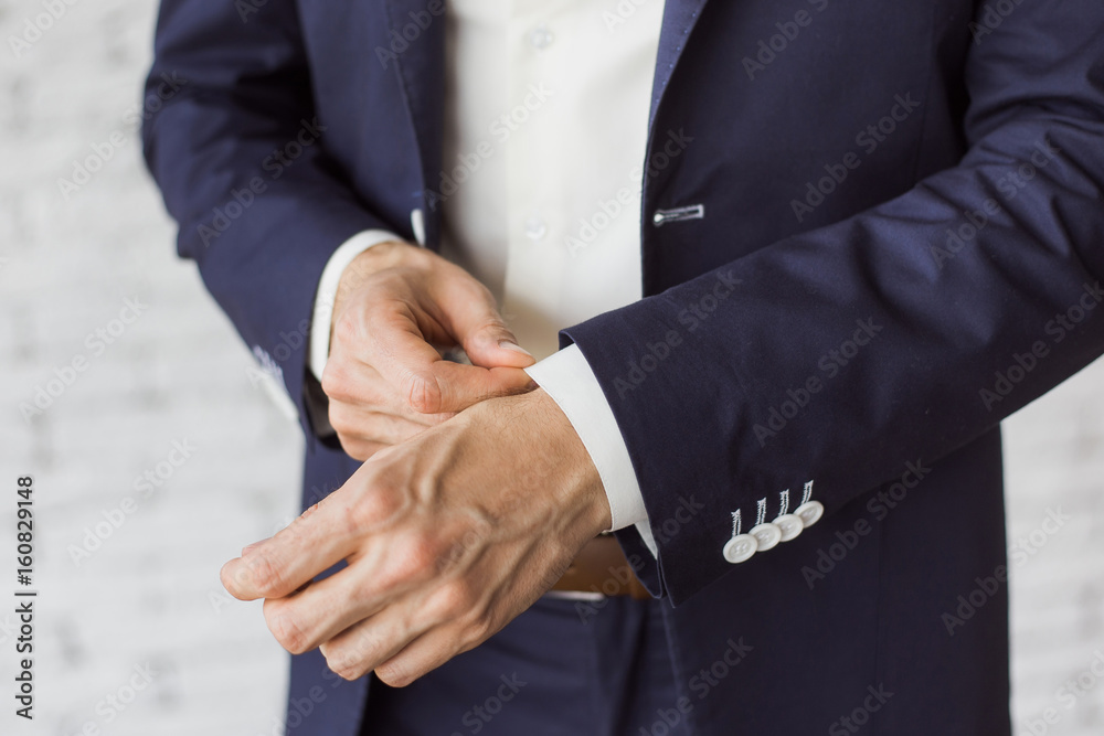 Obraz premium Closeup of elegant young fashion man dressing up for wedding celebration. Color close up image of male hands. Handsome groom dressed in modern blue formal suit, white shirt getting ready for event.
