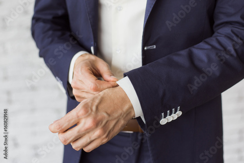 Closeup of elegant young fashion man dressing up for wedding celebration. Color close up image of male hands. Handsome groom dressed in modern blue formal suit, white shirt getting ready for event.