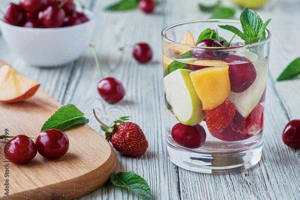 Fresh fruit detox water in a glass cup. Apple, cherry, peach, strawberry wooden table. Fresh fruit detox water in a glass cup. Apple, cherry, peach, strawberry wooden table.