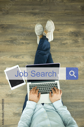 Young man sitting on floor with laptop and searching JOB SEARCH concept on screen