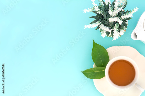 Top view shot of a hot cup of tea with green leaf and flower on blue background , Organic Tea ceremony time concept
