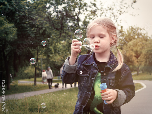 Little girl in Park blow bubbles. A lot of sun