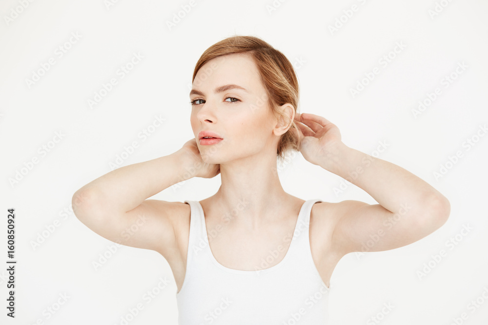 Young beautiful blonde girl with clean fresh skin looking at camera sitting at table over white background correcting hairstyle. Beauty and spa. Young beautiful blonde girl with clean fresh skin looking at camera sitting at table over white background correcting hairstyle. Beauty and spa.