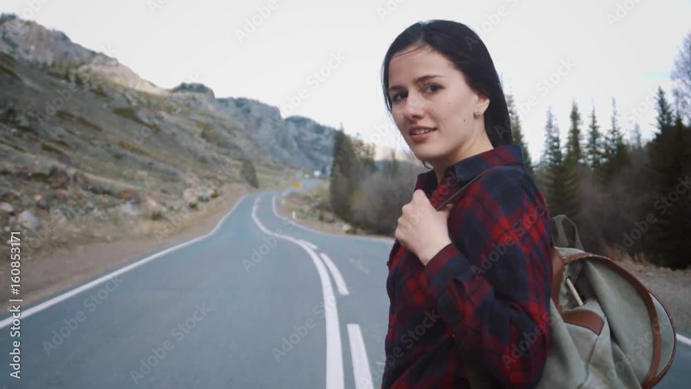 Traveler woman picking up her backpack. Backpacker woman lifts her bag from the road in the morning countryside background