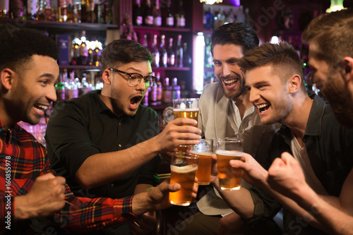 Happy male friends clinking with beer mugs in pub