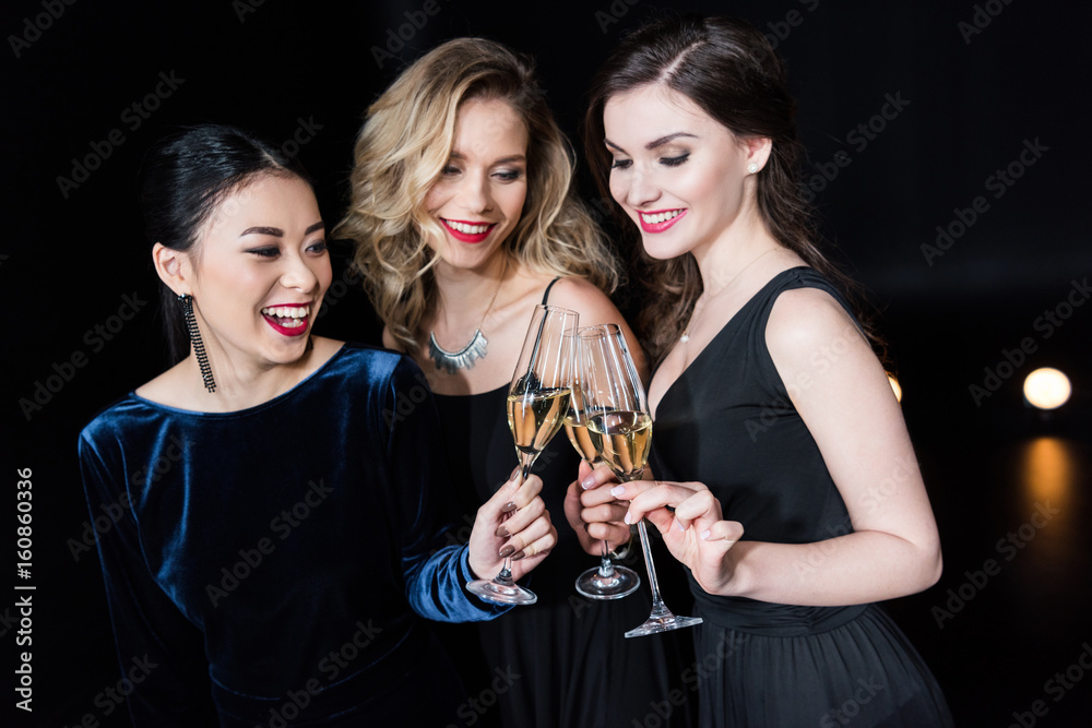 smiling women in stylish dresses clinking glasses with champagne