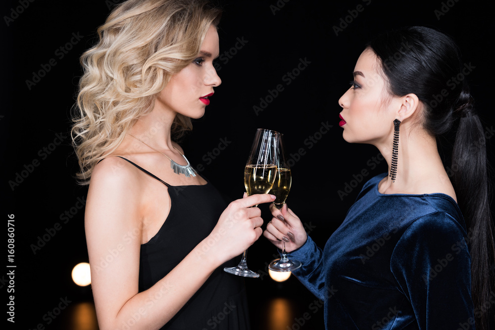 young glamour women in evening gowns clinking with champagne glasses at party young glamour women in evening gowns clinking with champagne glasses at party