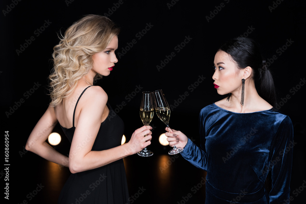 young glamour girls in evening gowns clinking with champagne glasses at party young glamour girls in evening gowns clinking with champagne glasses at party