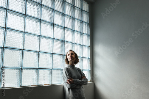 Young woman standing near window with folded hands