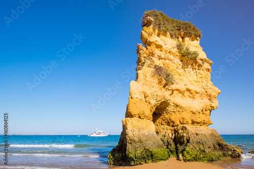 A large rock structure with facial features stands alone on the rocky coast of Lagos, Portugal