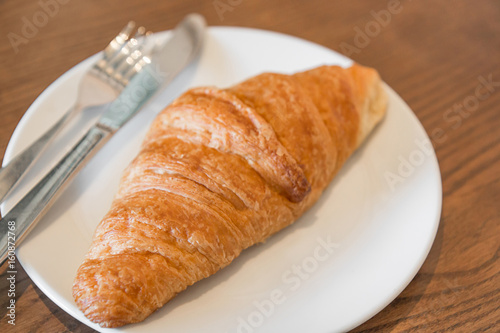 Warm fresh Croissants on a white plate with fork and knife in the coffee shop.(Selective focus with shallow depth of field)