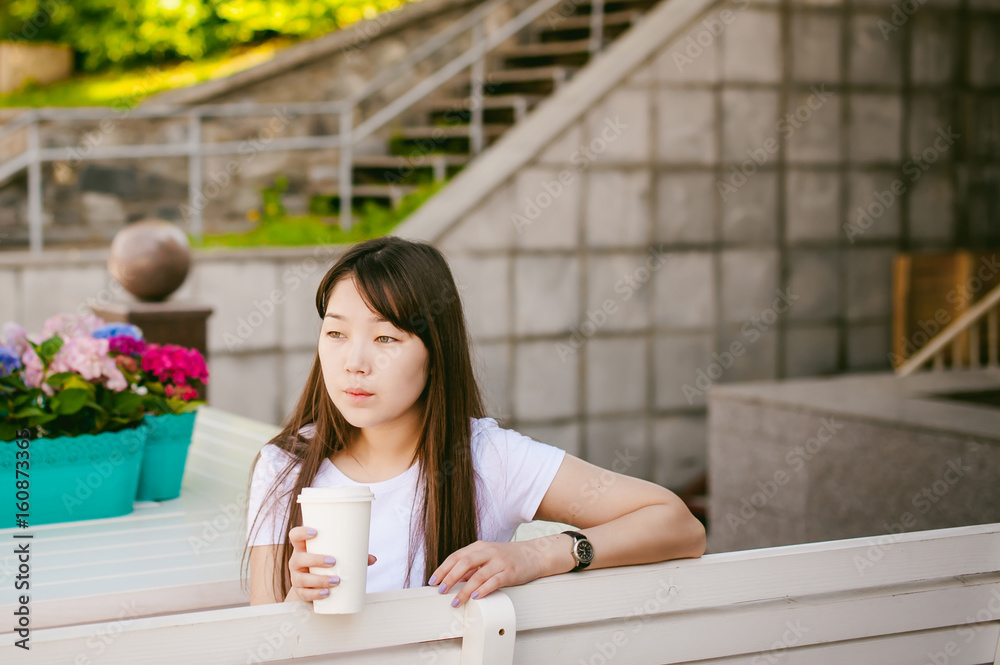 Cute asian young woman in summer cafe outdoors. girl In white T-shirt, with long hair in simple light cozy interior of restaurant Urban style, drinking coffee drink, sitting at table with flowers Cute asian young woman in summer cafe outdoors. girl In white T-shirt, with long hair in simple light cozy interior of restaurant Urban style, drinking coffee drink, sitting at table with flowers