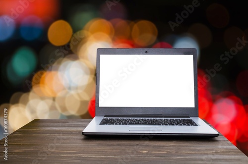Laptop notebook computer with white blank screen on wooden table with blurred night light bokeh background, selective focus, copy space