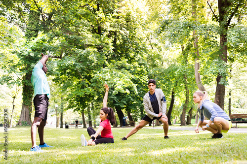 Group of young runners stretching and warming up in park.