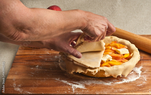 Female chef preparing to make a peach pie, by putting the dough top on to the pie in the ceramic pie pan