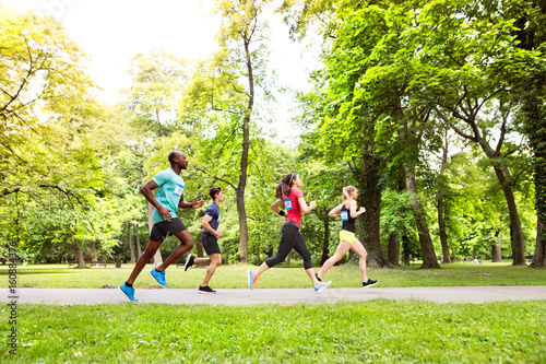 Group of young athletes running in green sunny park.